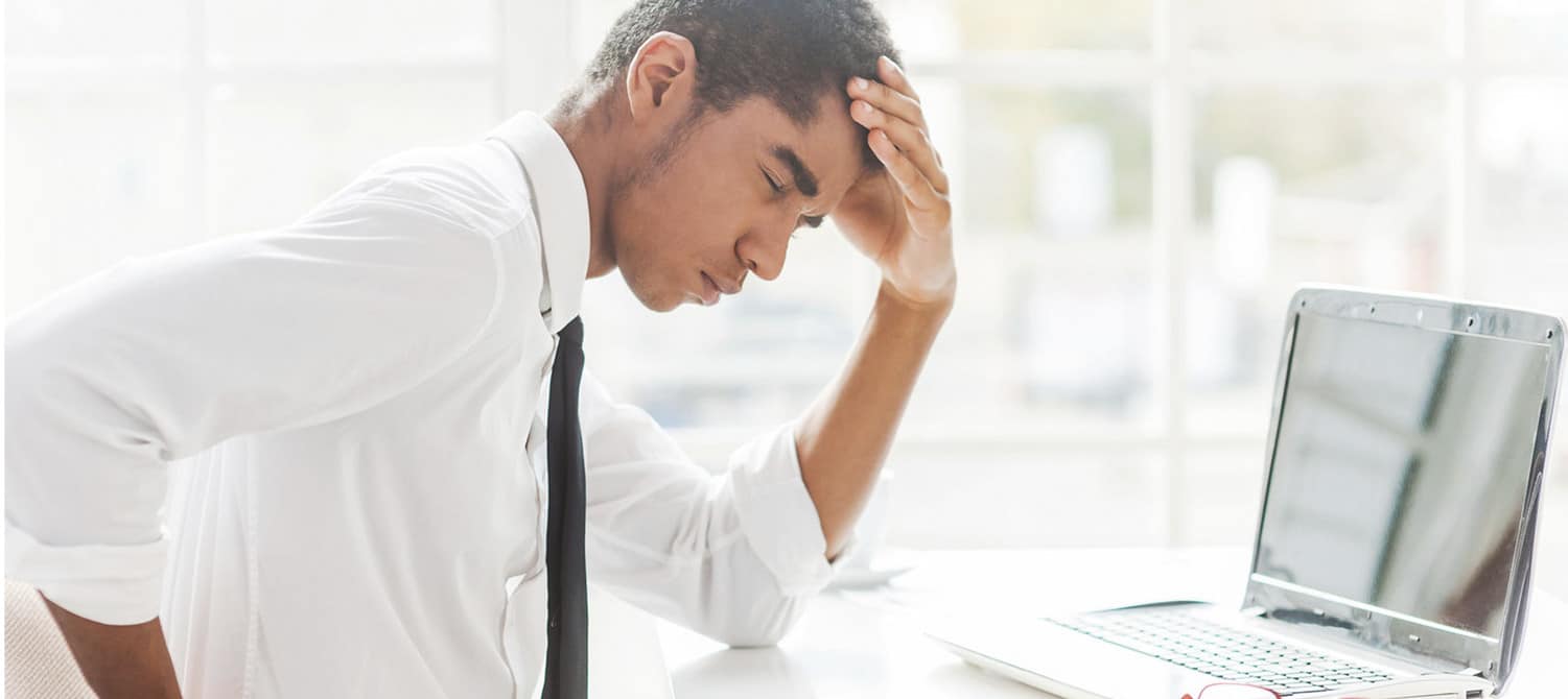 Man sitting at a desk with a laptop experiencing back pain