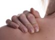 Close-up of a person’s hand gripping their shoulder, showing visible tension or discomfort in the upper back area.
