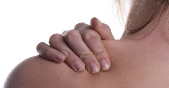 Close-up of a person’s hand gripping their shoulder, showing visible tension or discomfort in the upper back area.