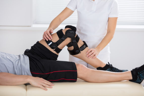 Woman physical therapist exercising man's leg during his first physical therapy appointment