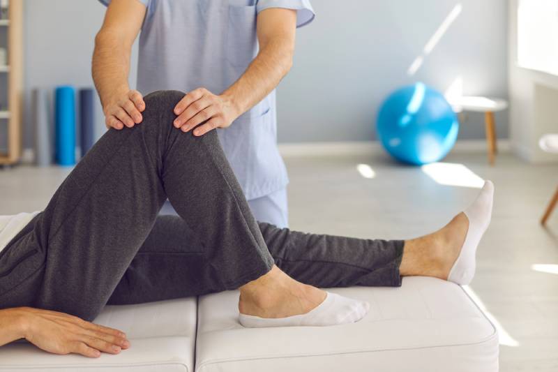 Physical therapist stabilizing the knee of a physical therapy patient who is laying flat on their back.