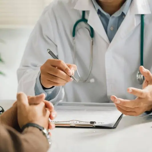 A man talks to a physician in a white coat about his physical therapy needs and coverage.