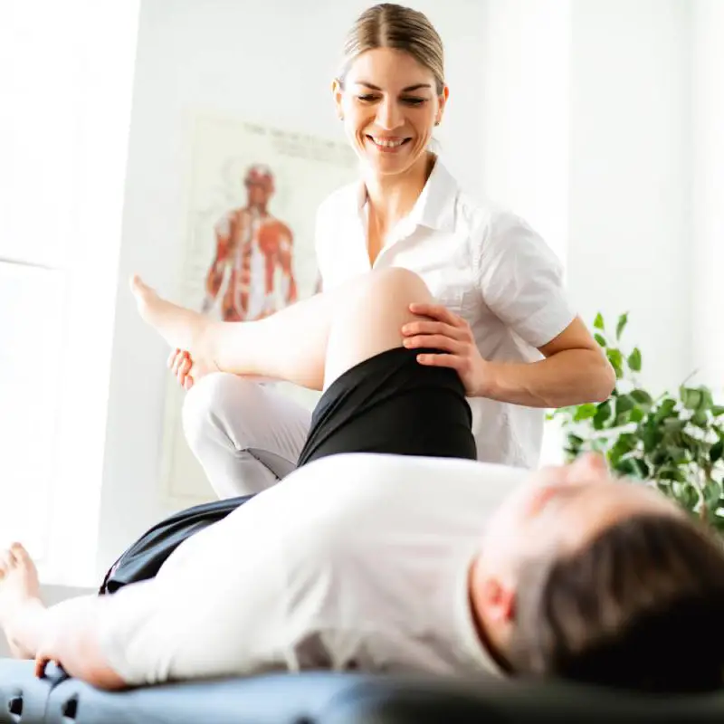 Female physiotherapist helps male patient do leg exercises.