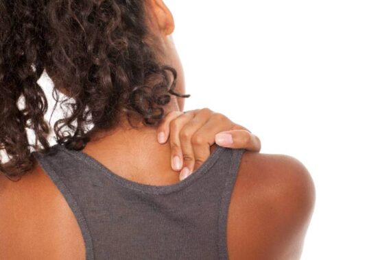 Close up of a Black woman holding her upper back in pain.
