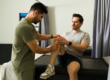 A physical therapist examines a seated man's knee in a clinic setting.
