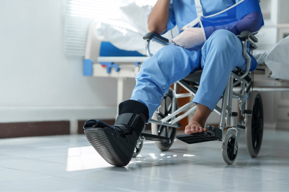 Patient wearing arm sling and walking boot sitting in wheelchair in hospital room