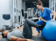 Female physical therapist helps a male patient with leg exercises including a blue exercise ball.