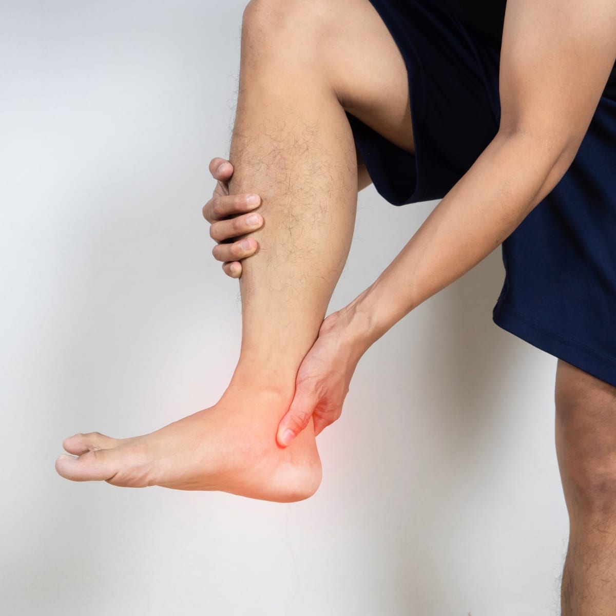 Person holding ankle experiencing pain, highlighted with red, indicating possible injury or inflammation.