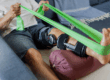 Senior man performing rehabilitation exercises using a green resistance band to aid in his knee recovery process at home. A physical therapy exercise with a leg brace.