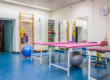 Empty room in physiotherapy clinic. Tables line the room with exercise balls underneath, and two shelves of smaller physical therapy equipment.