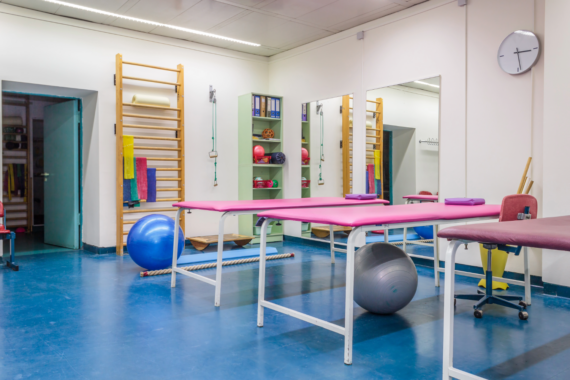 Empty room in physiotherapy clinic. Tables line the room with exercise balls underneath, and two shelves of smaller physical therapy equipment.