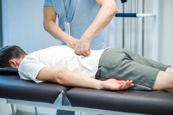 Manual therapist working with patient's back. The patient is laying face down on a table.