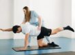 Physical therapist supervising a patient performing a bird-dog core exercise on a mat in a clinic.