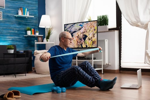virtual home therapy routine Older adult using a resistance band on an exercise mat during a virtual home therapy routine.